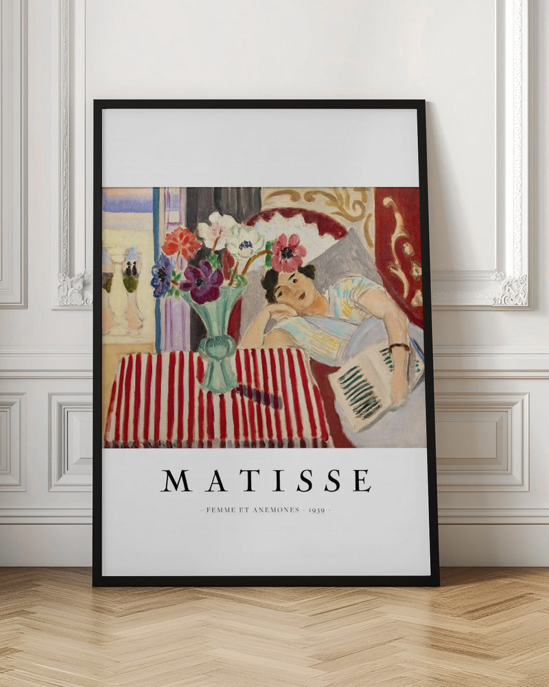 A poster featuring Henri Matisse's 1939 painting, 'Femme et Anemones'. The artwork depicts a woman in a colorful top reclining on a couch, holding a book. Beside her, on a red and white striped tablecloth, sits a vase filled with vibrant anemone flowers. The poster has a black frame and white matting, with 'MATISSE' printed below the image. Artwork