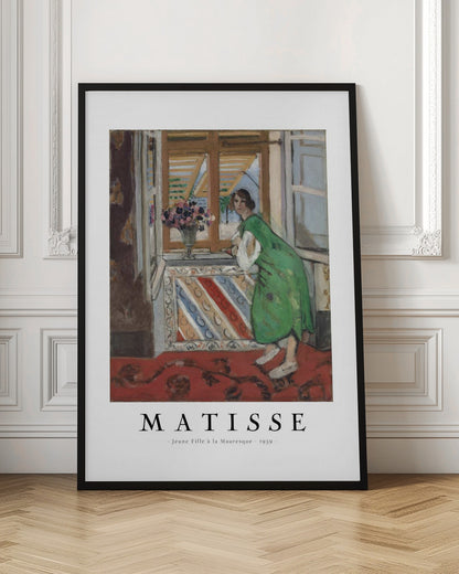 A framed art print of Henri Matisse's painting 'Jeune Fille à la Mauresque - 1939'. The painting shows a woman in a vibrant green dress standing in a room and looking out of an open window with shutters. A red patterned rug covers the floor, and a vase of flowers sits on the windowsill. Poster
