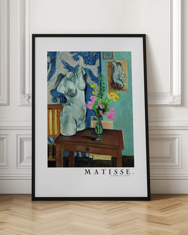 A framed art print of Henri Matisse's painting 'Le Torse en Plâtre'. The still life features a white plaster female torso sculpture next to a dark brown wooden table with a vase of pink and yellow flowers. The background consists of a blue and white patterned tapestry and a teal wall with a small framed nude drawing. Print