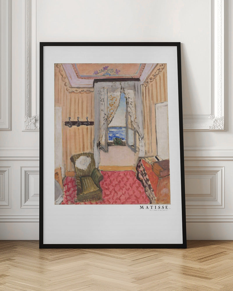 A framed print of a painting by Henri Matisse. The artwork depicts an interior room scene with peach-colored walls, a vibrant pink and red patterned rug, and an armchair. An open window with lace curtains offers a view of the blue sea. Decor