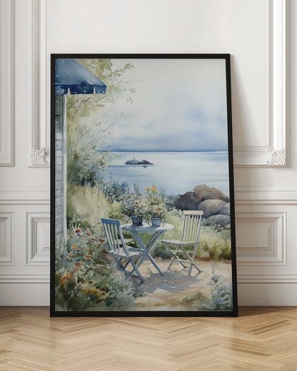 A watercolor painting of a tranquil coastal scene. A light blue bistro table and two matching chairs sit in a lush garden filled with flowers, overlooking a calm body of water. In the distance, a small island is visible under a soft, hazy sky. Part of a house with a blue awning can be seen on the left. Print
