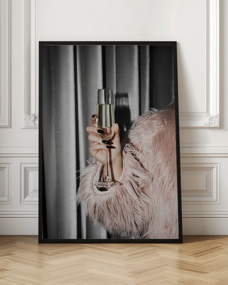 A close-up photograph of a woman's hand with black nail polish holding a tall, elegant flute of champagne. She is wearing a soft, shaggy pink faux fur coat, with a silver-gray curtain in the background, creating a luxurious and celebratory mood. Print