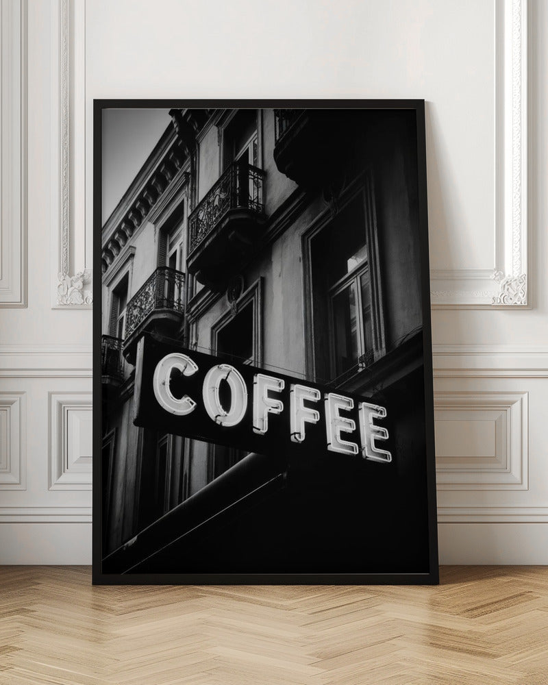 A dramatic, low-angle, black and white photograph of a bright white neon sign that reads 'COFFEE', mounted on a classic-style building with ornate balconies. Print