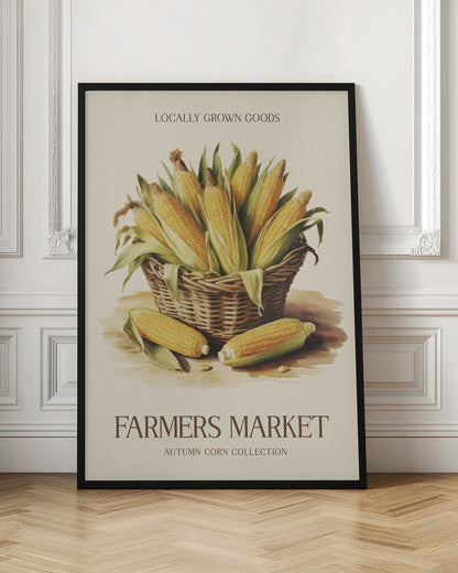 A vintage-style art print with a black frame featuring a wicker basket full of ears of corn. The poster has text that reads 'LOCALLY GROWN GOODS' at the top and 'FARMERS MARKET AUTUMN CORN COLLECTION' at the bottom. The background is a light cream color. Artwork