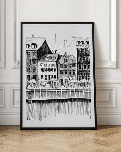 A black and white ink line drawing of a charming European city scene along a canal. Tall, narrow buildings with gabled roofs line the waterfront, in front of which is a bustling pier with outdoor cafes filled with people under umbrellas. The water's reflection is illustrated with simple vertical lines. The artwork is framed in black. Wall Art