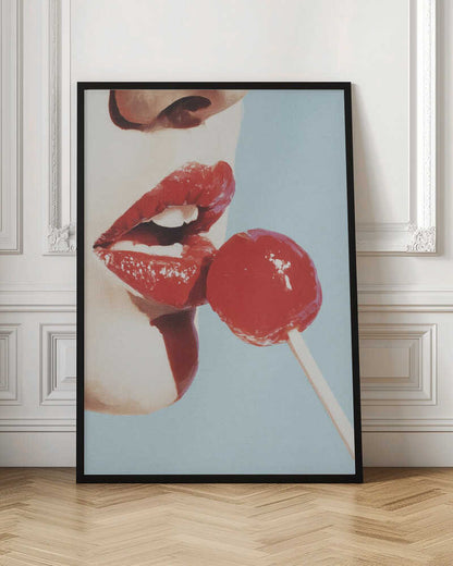 A pop art painting in a black frame, featuring a close-up of a woman's face in profile with bright red lipstick. Her lips are parted as she touches them to a round, red lollipop against a solid light blue background. Print