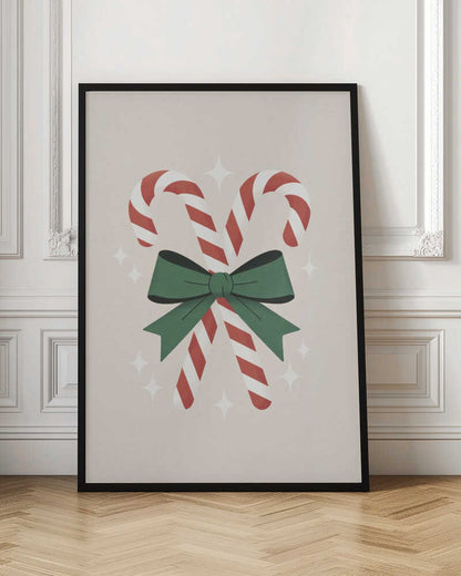 An illustration of two red-and-white striped candy canes crossed and tied together with a large green bow. The background is a soft beige color with small, white, four-pointed star sparkles. The artwork is shown in a black frame. Decor