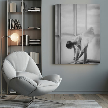 A black and white photograph of a ballerina in a white tutu, bending over to tie her pointe shoe in front of a large, bright window. The motion of her tutu is captured in a graceful blur. Print