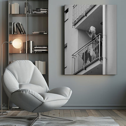 A black and white photo of a woman with a towel on her head, smoking a cigarette on an apartment balcony. The low-angle shot captures her leaning on the metal railing, with smoke drifting from the cigarette. Print
