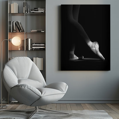 A dramatic black and white photograph showing the lower legs and feet of a ballet dancer, with one foot gracefully en pointe, highlighted by strong side lighting against a deep black background. Decor