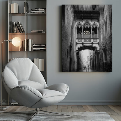 A moody, vertical black and white photograph of an ornate Gothic-style bridge connecting two stone buildings over a narrow alleyway. Below the arch of the bridge, the wet street stretches into the distance where two figures are walking away. Decor