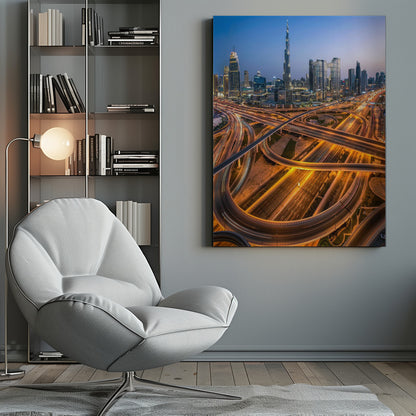 A long-exposure, aerial photograph of the Dubai skyline at dusk. The iconic Burj Khalifa stands tall in the center, surrounded by other illuminated skyscrapers against a deep blue twilight sky. In the foreground, a complex web of highways and overpasses glows with the orange and white light trails of moving traffic. Decor