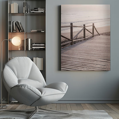 A wooden boardwalk with a rustic log fence leads down to a sandy beach with gentle waves lapping at the shore under a soft, hazy sunrise or sunset. Decor