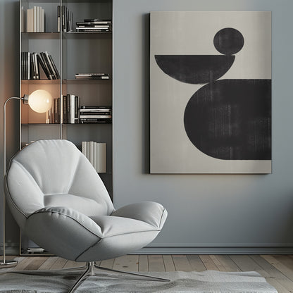 A minimalist abstract artwork featuring three charcoal black shapes stacked against a light beige textured background. At the bottom is a large, rounded shape, on which a semi-circle is balanced. A smaller, full circle rests on top of the semi-circle, creating a sense of precarious balance. The piece is enclosed in a simple black frame. Decor