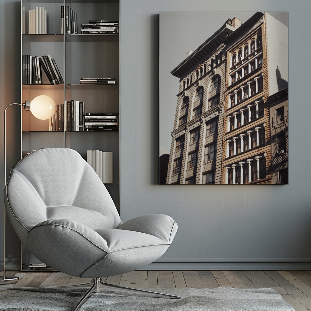 A low-angle, sunlit photograph of two ornate, multi-story historic buildings against a pale sky, framed in black. The detailed facades feature arched windows and decorative columns, with warm light creating strong shadows. Poster