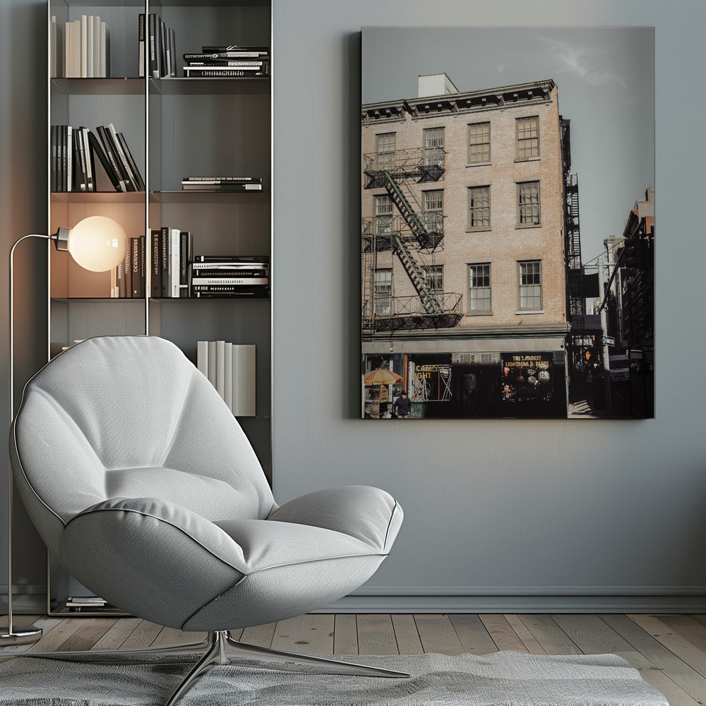 A low-angle, desaturated photograph of a classic brown brick building in a city, featuring multiple windows and a black metal fire escape zigzagging up the side. The sky is a pale, hazy blue, and the ground floor has dark storefronts. Decor