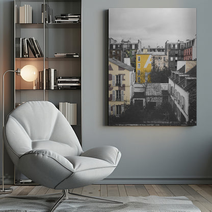 A framed, vertical photograph with selective color, showing a dense cluster of Parisian-style buildings under an overcast sky. Most of the image is in black and white, but one building is a vibrant yellow with a large white 'A' painted on it, creating a striking focal point. Wall Art