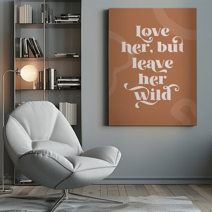 A framed typography poster with a terracotta brown background. In the center, the quote 'love her, but leave her wild' is written in a stylized, decorative, cream-colored font. Faint, lighter brown abstract shapes are visible in the background. Decor
