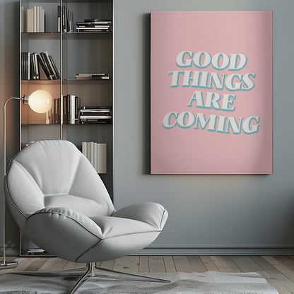 A framed poster with a light pink background featuring the motivational phrase 'GOOD THINGS ARE COMING'. The text is in a white, retro-style serif font with a light blue drop shadow, giving it a three-dimensional effect. Poster