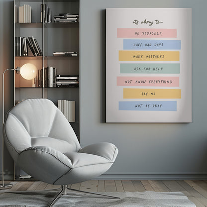 A framed inspirational poster with a white background. At the top, in a black handwritten font, it says 'it's okay to...'. Below is a list of affirmations, each on a different colored pastel rectangle: 'BE YOURSELF' on pink, 'HAVE BAD DAYS' on blue, 'MAKE MISTAKES' on yellow, 'ASK FOR HELP' on green, 'NOT KNOW EVERYTHING' on pink, 'SAY NO' on yellow, and 'NOT BE OKAY' on blue. Poster