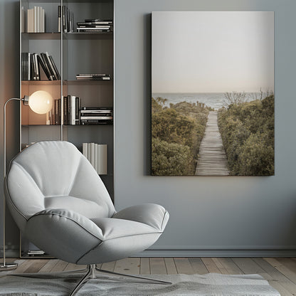 A vertical photograph of a weathered wooden boardwalk leading through dense coastal greenery towards the ocean under a pale, hazy sky, framed in black. Wall Art