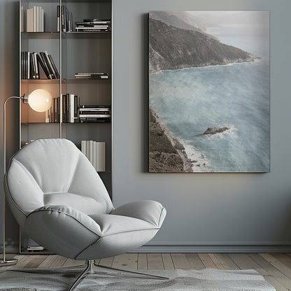 A high-angle photograph of a rugged, green coastline meeting a misty, light-blue ocean. The hazy atmosphere softens the view of the distant mountains and the waves crashing against the rocky shores. Poster