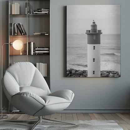 A framed, black and white photograph of a tall, cylindrical lighthouse standing on a rocky shore. The lighthouse is dark grey on its upper section and white on the lower, with the ocean and a grey sky in the background. Print