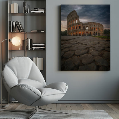 A low-angle view of the Roman Colosseum at dusk, with its arched windows glowing with warm orange light under a dramatic, stormy sky. An ancient cobblestone road leads towards the iconic amphitheater. Print
