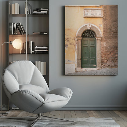 A vertical shot of a rustic European street scene featuring a dark green arched wooden door set into a stone frame. The building's facade is a mix of peeling yellow ochre plaster and exposed red brick. Above the door is a marble plaque that reads 'SALITA RI DEL GRILLO', and the ground is paved with grey cobblestones. Wall Art