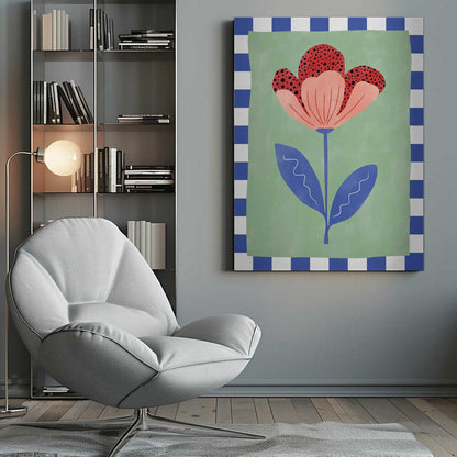 A framed illustration of a stylized flower with red polka-dotted and pink petals. The flower has a blue stem and two blue leaves, set against a sage green background with a blue and white checkered border. Artwork