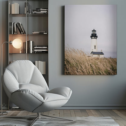 A framed photograph of a white lighthouse with a black top, set against a muted, overcast sky. The foreground is filled with tall, wild beige grass blowing in the wind, partially obscuring the base of the lighthouse. Decor