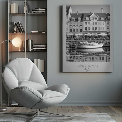 A black and white framed poster of Nyhavn in Copenhagen. The photograph features classic Danish buildings lining a canal, with a sailboat moored in the water. The buildings and boat are perfectly reflected in the still water. At the bottom, text reads 'KØBENHAVN', 'Nyhavn', and 'DANMARK'. Wall Art