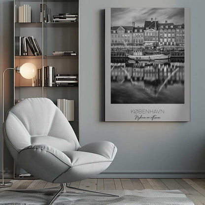 A black and white poster of Nyhavn harbor in Copenhagen at night. Historic buildings with glowing windows line the canal, and their lights create shimmering reflections in the water. A boat is docked in the foreground. The poster has text at the bottom that reads 'KØBENHAVN, Nyhavn om aftenen, DANMARK'. Poster