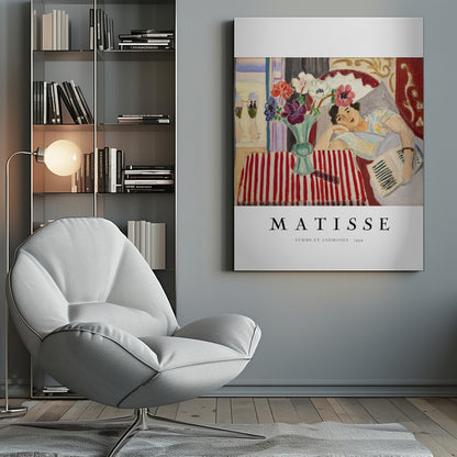 A poster featuring Henri Matisse's 1939 painting, 'Femme et Anemones'. The artwork depicts a woman in a colorful top reclining on a couch, holding a book. Beside her, on a red and white striped tablecloth, sits a vase filled with vibrant anemone flowers. The poster has a black frame and white matting, with 'MATISSE' printed below the image. Artwork