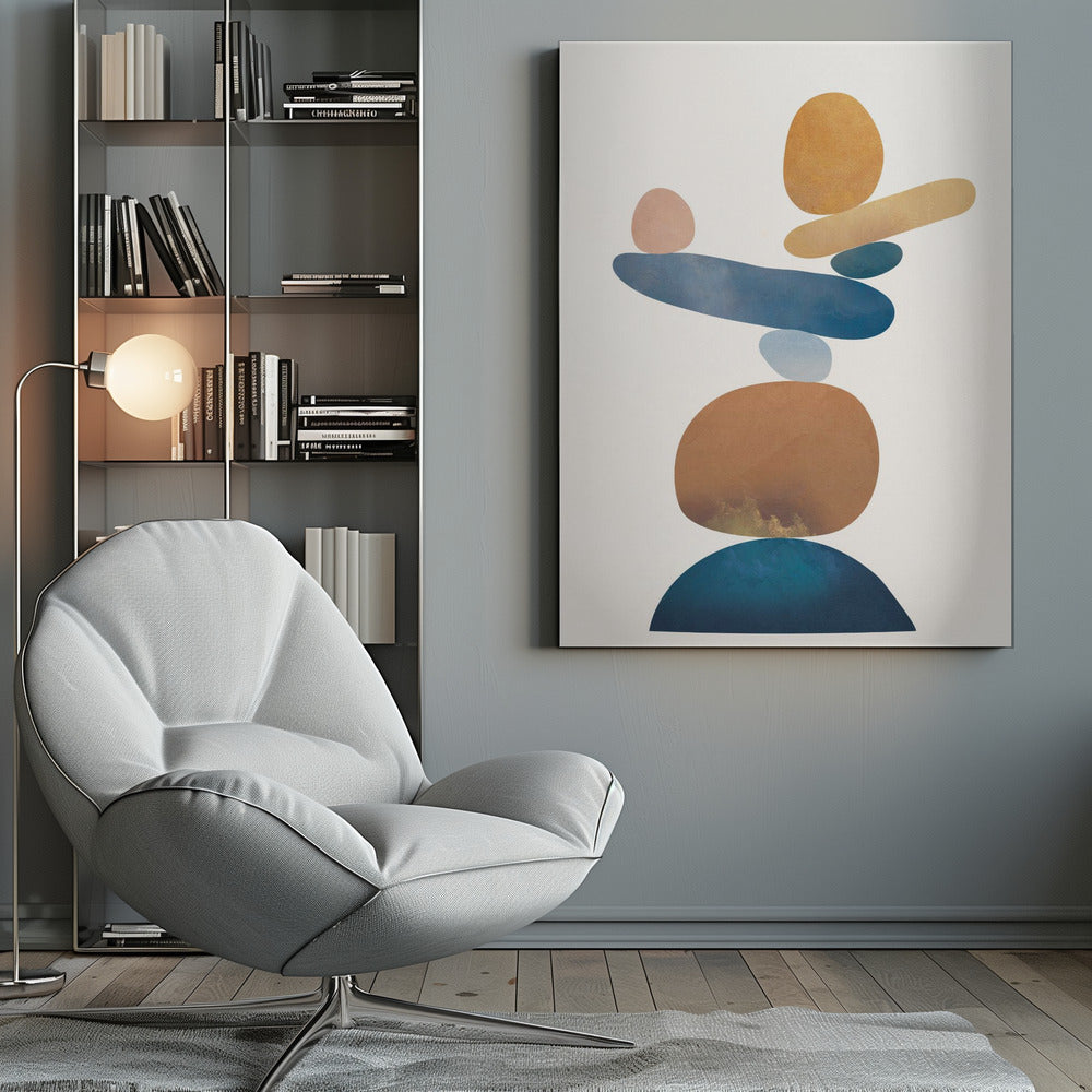 An abstract art print in a thin black frame featuring a stack of colorful, organic shapes resembling balanced stones against a white background. The forms are in various shades of blue, earthy brown, ochre, and a muted pink, creating a sense of calm and equilibrium. Artwork