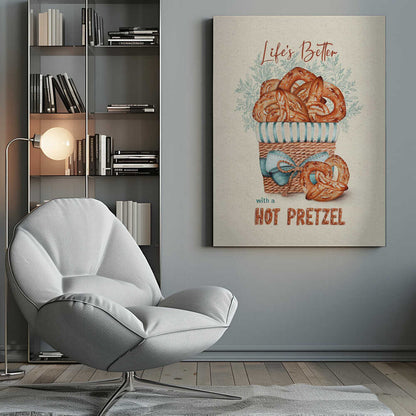 A vintage-style framed artwork featuring a watercolor illustration of a wicker basket overflowing with golden-brown pretzels. The text reads 'Life's Better with a HOT PRETZEL' in a warm brown font against a cream-colored textured background. A blue ribbon is tied around the basket, and light blue foliage is visible behind it. Poster