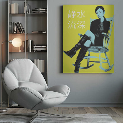 A pop art style poster with a stark yellow background featuring a woman in a black jacket and tall black boots sitting in a rocking chair. The image is rendered in high contrast with black and light blue tones. The woman is looking at the viewer with her chin on her hand. To the left, there are four large white Japanese characters. The entire piece is framed in black. Print