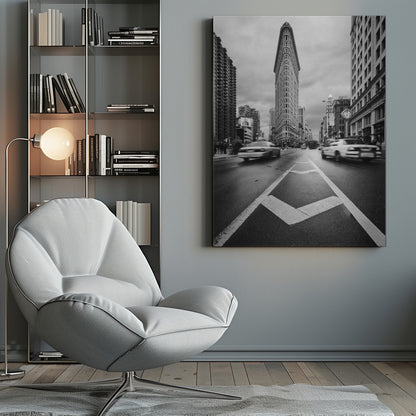 A dynamic black and white, low-angle photograph of the iconic Flatiron Building in New York City. The street in the foreground has bold white lines leading the eye to the building, while cars on either side are blurred with motion, capturing the city's fast pace under a cloudy sky. Decor