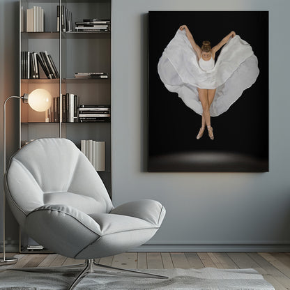 A high-angle studio photograph of a graceful ballet dancer suspended mid-air against a solid black background. She wears a white leotard and pointe shoes, with her legs crossed. Her arms are outstretched, holding a large, flowing white fabric that creates a shape like wings around her. Decor