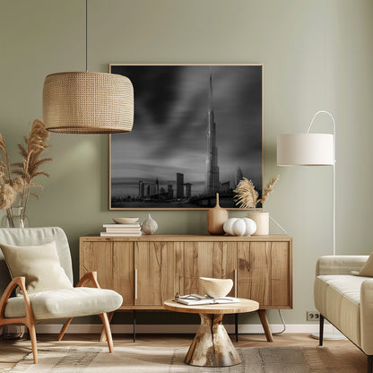 A framed, long-exposure black and white photograph of the Dubai skyline, featuring the iconic Burj Khalifa. The sky has a dramatic, streaky appearance from the long exposure, contrasting with the sharp details of the modern architecture. A bridge crosses the water in the foreground. Print