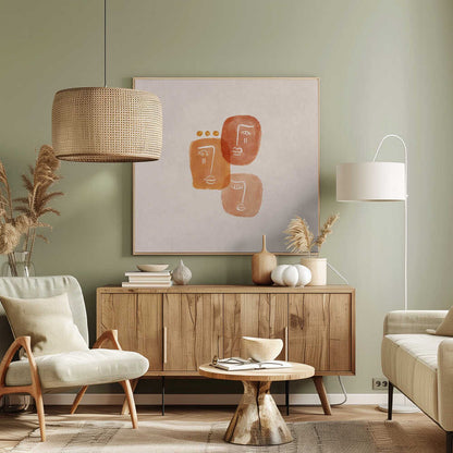 A minimalist abstract painting in a light wood frame, featuring three stylized faces rendered in orange and terracotta watercolor shapes with simple white line art on a textured beige background. One face is adorned with three small gold dots above it. Artwork