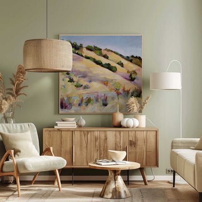 An impressionist oil painting of golden, rolling hills dotted with green shrubs under a pale blue sky, framed in light wood.