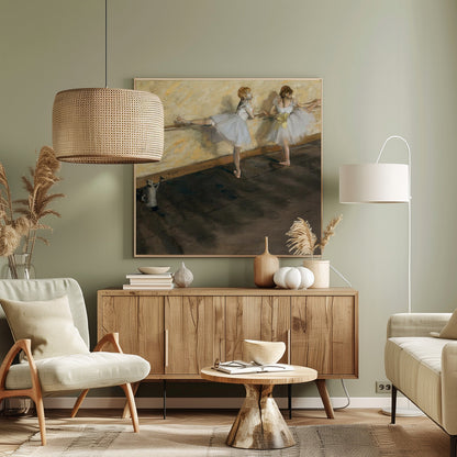 A framed impressionist painting by Edgar Degas depicting two ballet dancers in white tutus practicing at a barre. The studio has a yellow wall and a dark brown wooden floor. One dancer stretches her leg on the barre while the other stands beside her. Artwork