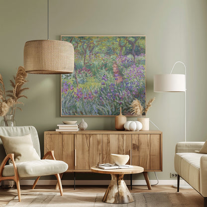 An impressionist painting by Claude Monet, 'The Artist's Garden at Giverny,' set in a light wood frame. The artwork depicts a lush, vibrant garden with a path winding through it. The foreground is dominated by purple irises and tall green leaves, while the background features trees and a mix of colorful flowers in shades of red, yellow, and white, all rendered with visible, textured brushstrokes. Print