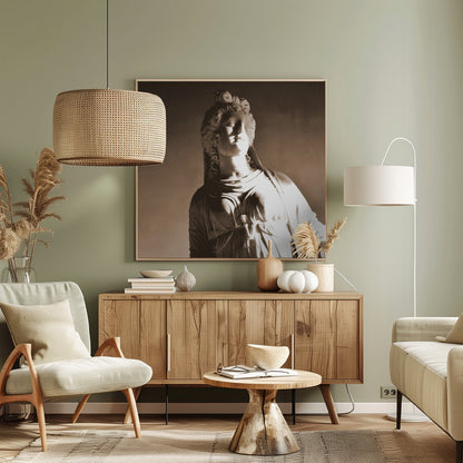 A framed, sepia-toned photograph of a classical marble bust of a woman. She looks upwards and to the side, illuminated by a strong light that casts dramatic shadows across her face and draped clothing. The photo is enclosed in a simple, light wood frame. Print