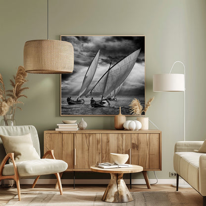A dramatic black and white photograph of a fleet of traditional wooden sailboats with large, billowing sails racing on a choppy sea under a dark, stormy sky. The image is presented in a light wood frame. Print