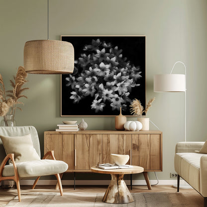 A moody black and white close-up photograph of a cluster of small, delicate star-shaped flowers against a solid black background, presented in a light brown wooden frame. Poster