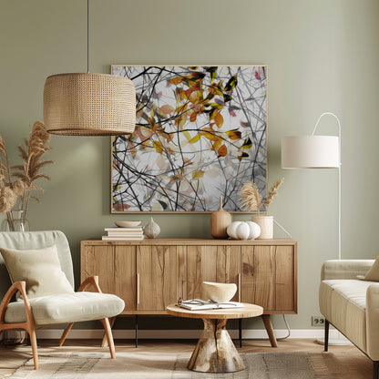 An abstract artwork in a light wood frame featuring a dense tangle of black and grey branches interwoven with soft, glowing autumn leaves in shades of orange and yellow against a white background. Poster