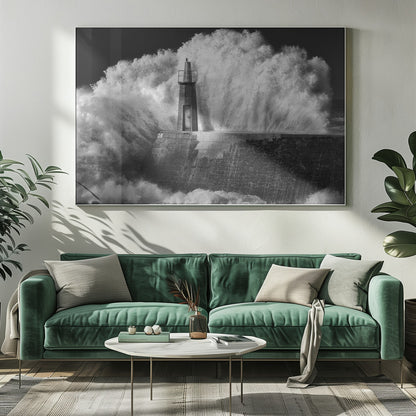 A dramatic black and white photograph of a massive wave crashing against a stone pier and a small lighthouse. The white foam of the wave towers over the structure, creating a powerful and dynamic scene against a dark sky, all enclosed in a silver frame. Poster
