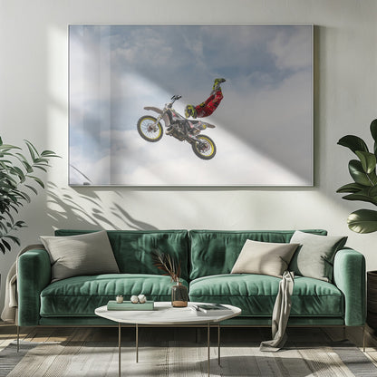 A motocross rider in red and yellow gear performs a high-flying stunt, arching their back while upside down in the air next to their dirt bike, set against a backdrop of a blue sky with white clouds and enclosed in a silver frame. Poster